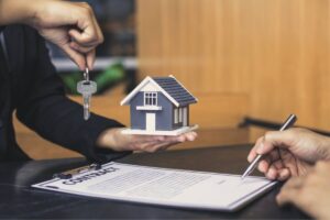 Firmare contratto, mano tiene chiave e piccola riproduzione di casa