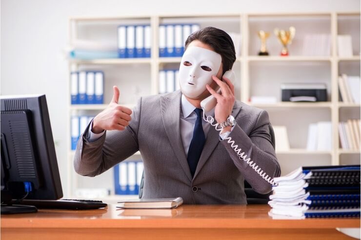 Uomo vestito in giacca e cravatta con maschera, al telefono da un ufficio