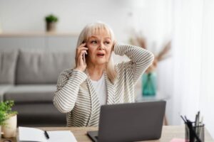 Donna al telefono mano dietro la nuca, PC davanti a lei