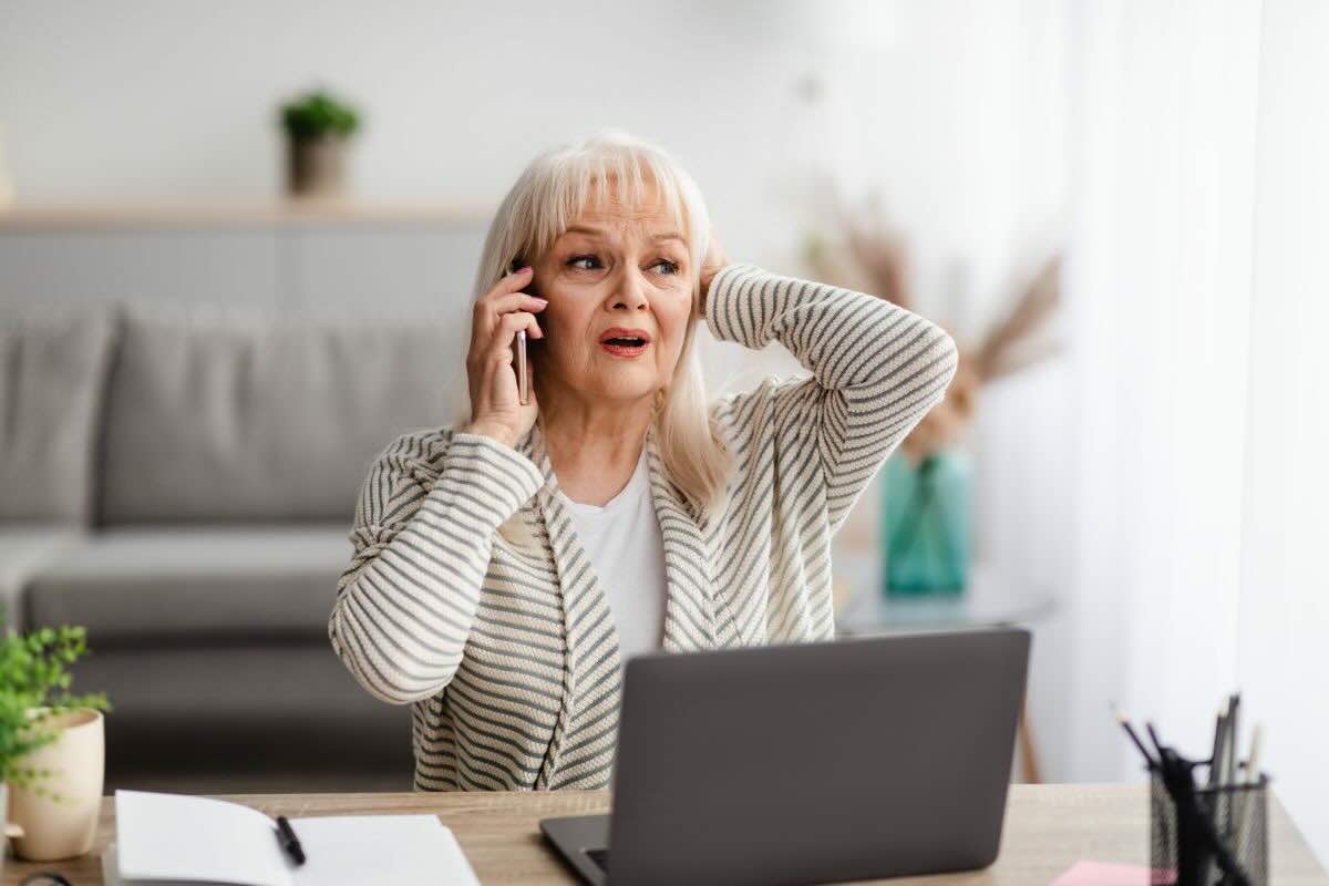 Donna al telefono mano dietro la nuca, PC davanti a lei