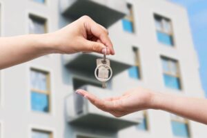 Due mani che si passano un mazzo di chiavi, sullo sfondo un condominio