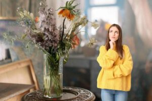 un salone che ha un mazzo di fiori appassiti ed una donna dubbiosa accanto