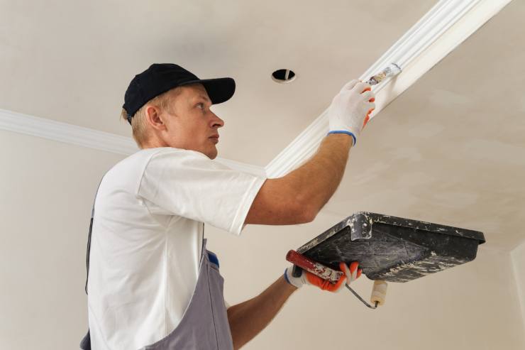 Un uomo che sta lavorando e ritinteggiando un soffitto