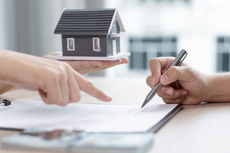 Persona fa firmare un contratto, ha in mano una casa in miniatura