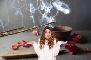 Una donna dubbiosa in primo piano con dell'incenso sullo sfondo