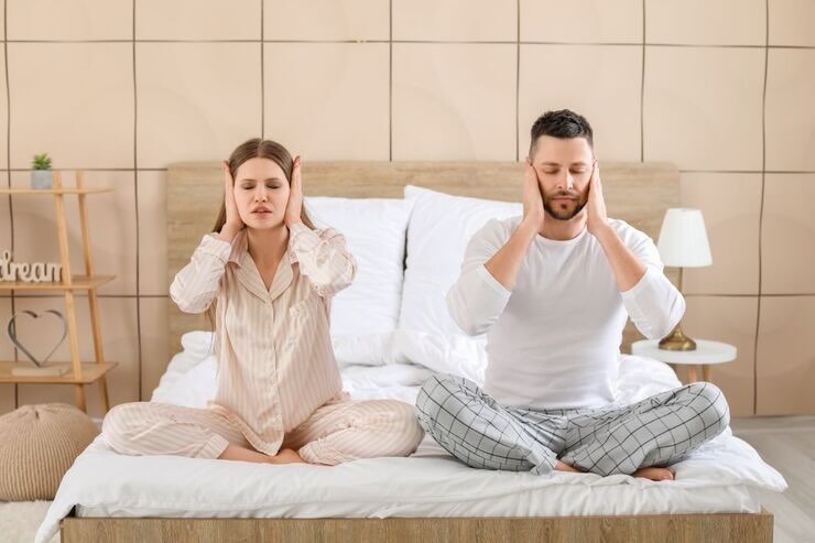 Uomo e donna seduti sul letto si tappano orecchie