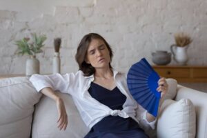 Donna sul divano accaldata sventola ventaglio