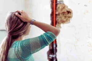 donna preoccupata di fronte a danno su paretet
