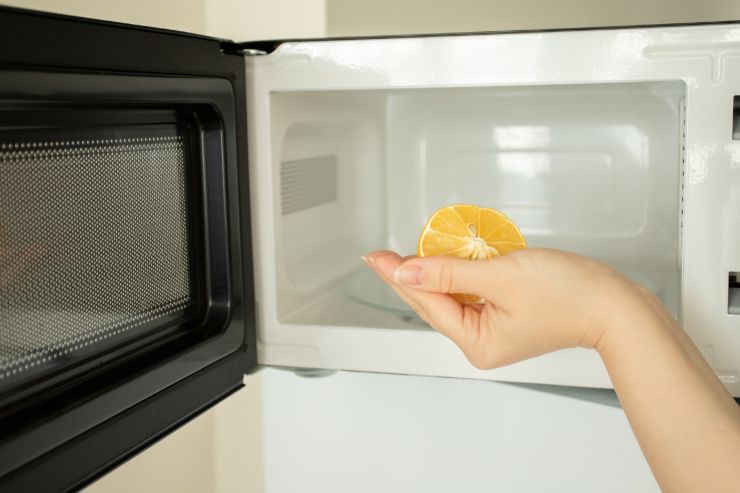 un microonde aperto con una mano che sta mettendo all'interno del microonde un mezzo limone
