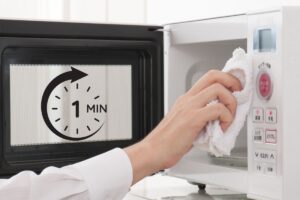 una mano che pulisce un microonde con un panno e un timer di un minuto sulla sinistra