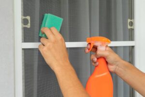 una persona che pulisce le zanzariere con una spugna ed uno spruzzino