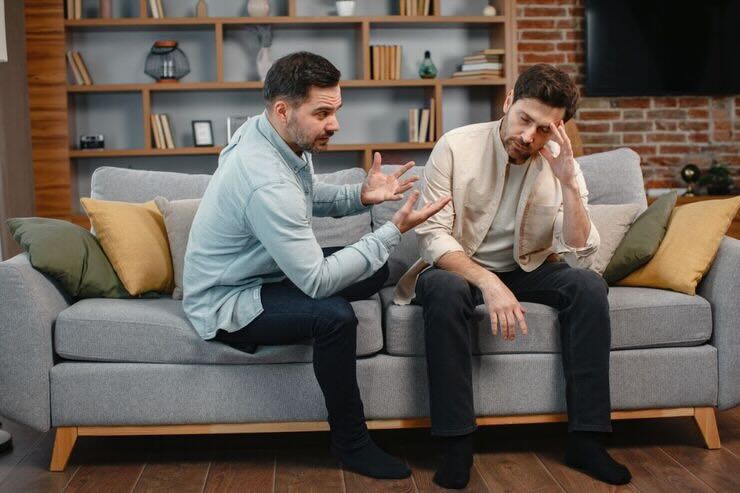 Due uomini seduti sul divano, uno discute sull'altro che lo ascolta con mano sul viso