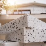 Una foto che ha come sfondo una casa e in primo piano il materiale per realizzare il cappotto termico