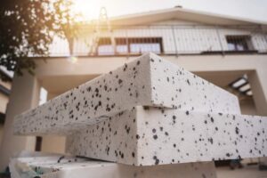 Una foto che ha come sfondo una casa e in primo piano il materiale per realizzare il cappotto termico