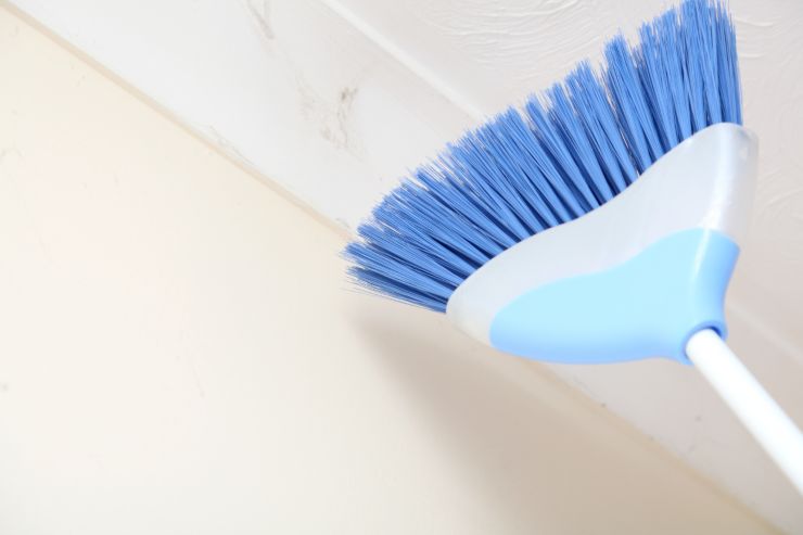 Una persona che sta rimuovendo delle ragnatele dal soffitto con una scopa