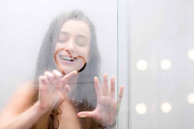 una ragazza in doccia che fa un cuore sul vetro della doccia 