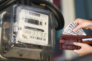 Un contatore elettrico con a destra delle mani che prendono dei soldi dal portafoglio
