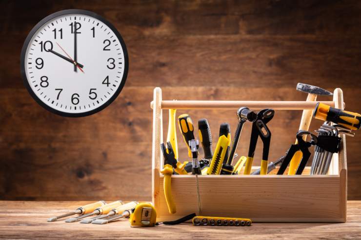 Un tavolo con sopra gli una cassetta degli attrezzi e con un orologio a muro sulla parete