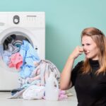 Una lavatrice aperta con i panni ed una donna che si tappa il naso dalla puzza