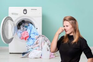 Una lavatrice aperta con i panni ed una donna che si tappa il naso dalla puzza