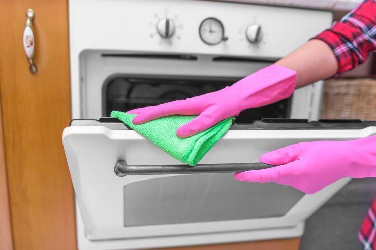 Una persona che sta lavando il forno con una pezzetta