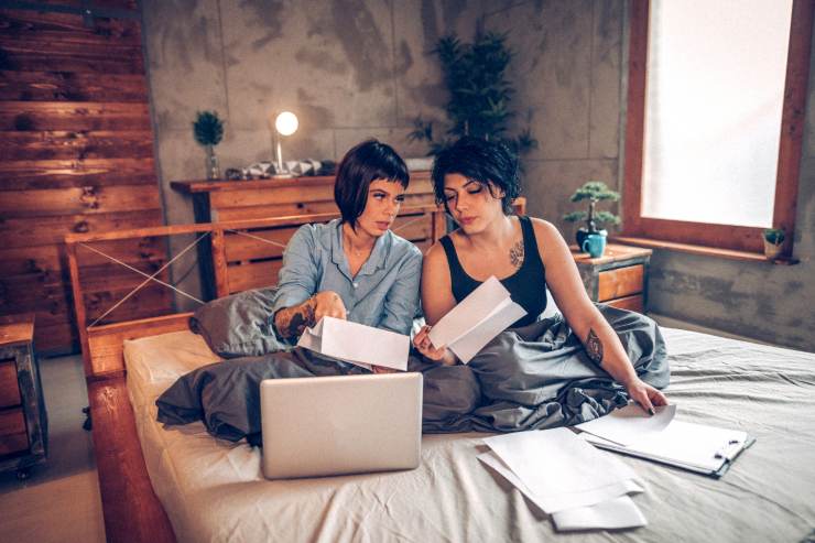 Due ragazze sul letto che parlano tra loro delle spese che devono sostenere