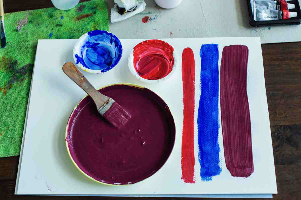 ciotole con tre colori, pennello e strisce di pittura rosso blu e viola