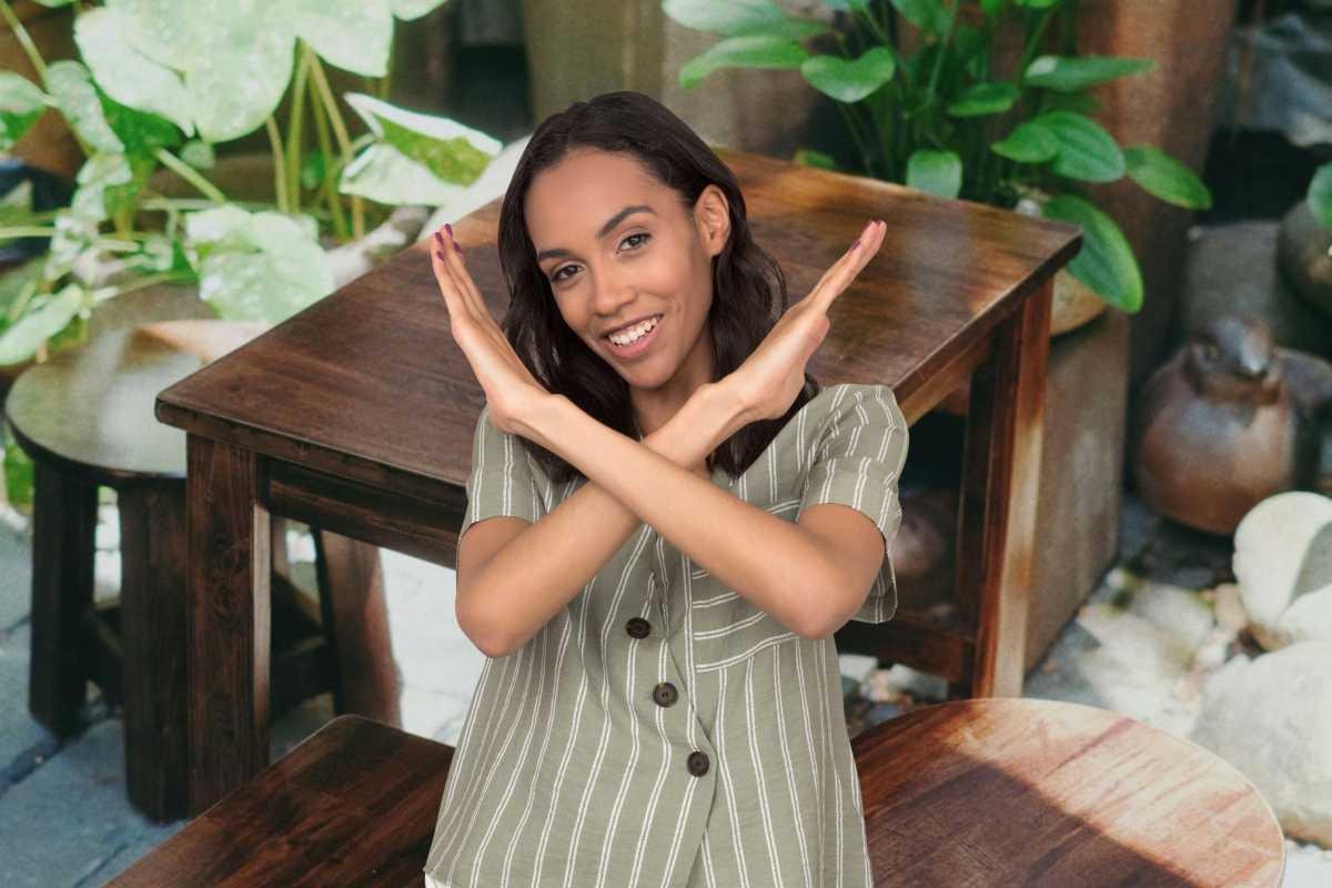 Sedia e tavolino di legno, davanti ragazza che fa una X con le braccia