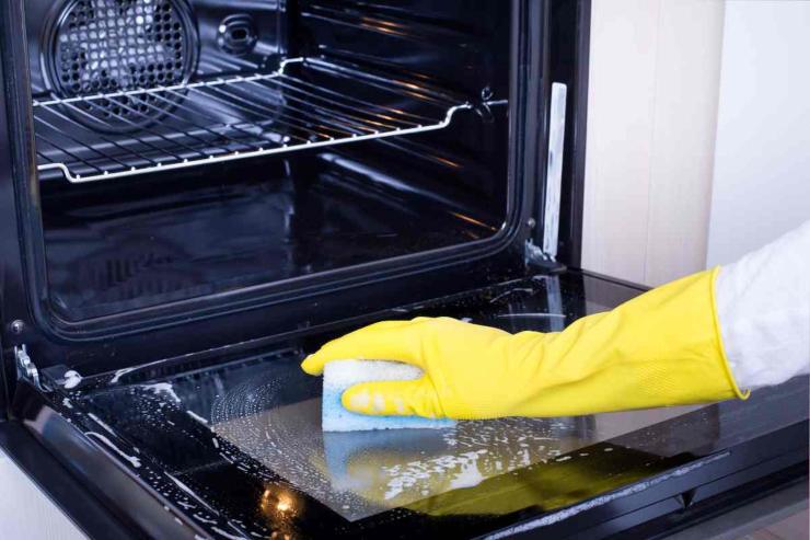 mano che pulisce il forno con spugnetta