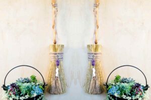 Scopa da strega decorativa per Halloween appoggiata a un muro vicino a un calderone con piante grasse