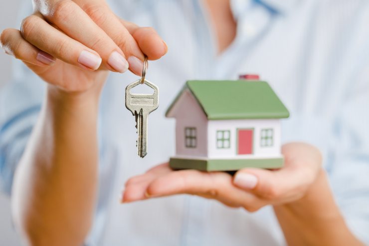 Una donna che tiene in una mano una miniatura di una casa e delle chiavi