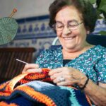 Una signora anziana che sta ricamando a maglia ed in alto a sinistra un gomitolo di lana in alto a sinistra