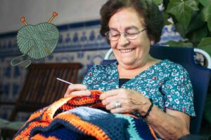 Una signora anziana che sta ricamando a maglia ed in alto a sinistra un gomitolo di lana in alto a sinistra