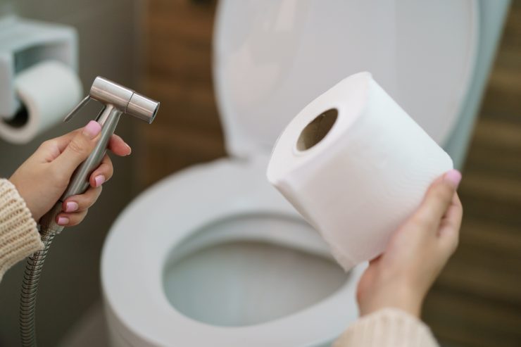 Una persona in bagno che tiene in mano della carta igienica e una doccetta da bidet