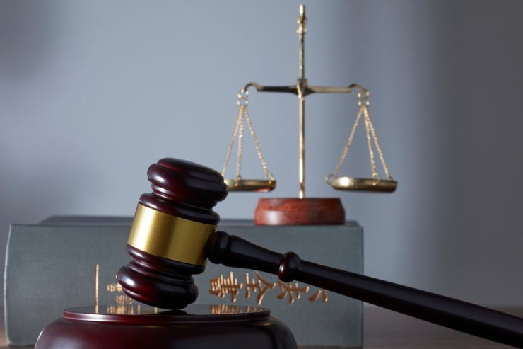 Un libro di legge con sopra una bilancia e in primo piano un martello da giudice