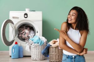 Una lavatrice con dei panni che cadono in una cesta ed una ragazza contenta che indica la lavatrice