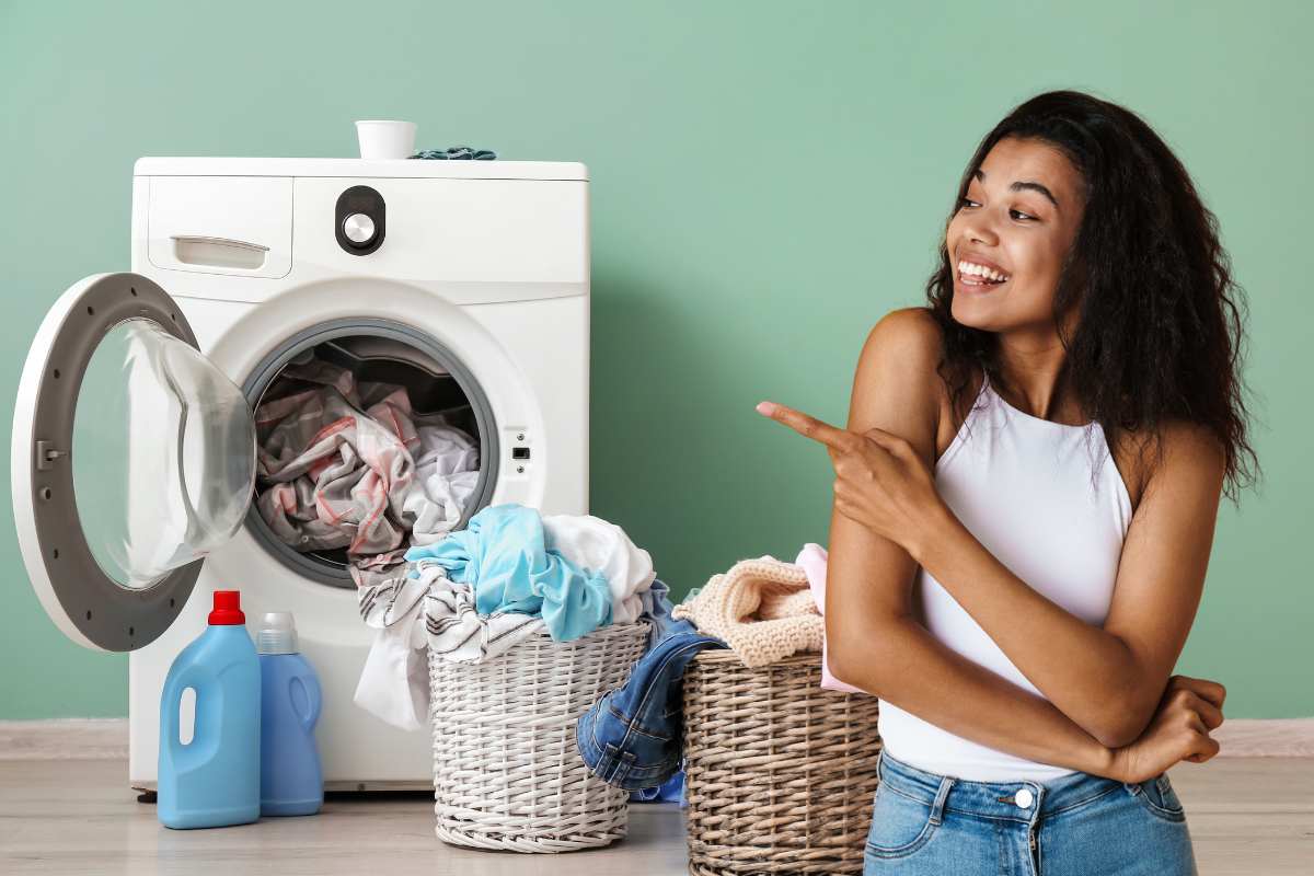 Una lavatrice con dei panni che cadono in una cesta ed una ragazza contenta che indica la lavatrice