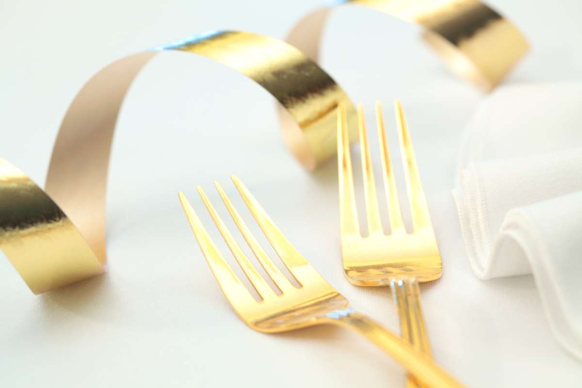 posate dorate vicino a tovagliolo bianco e nastro color oro
