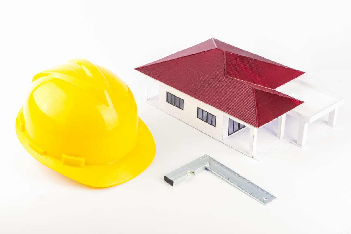 un modellino di edificio con tetto a padiglione, una livella e un casco da cantiere