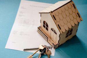 Modellino di una casa, insieme alle chiavi e a un documento
