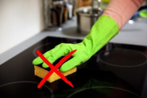 mano con guanto verde che pulisce piano ad induzione e x rossa sulla spugnetta