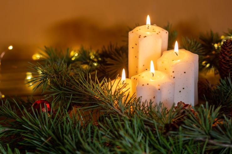 Delle candele natalizie circondate da dei rami di pino
