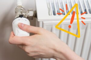 Una persona che accende i termosifoni e un segnale di pericolo in alto a destra