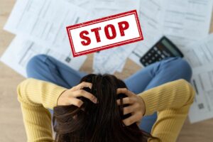 Una ragazza con le mani tra i capelli mentre guarda varie bollette e una scritta "stop" in primo piano
