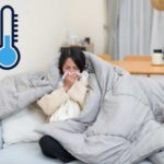 Una ragazza sul divano che sente freddo e si soffia il naso ed in altro a sinistra un termometro che segna una temperatura ghiacciata
