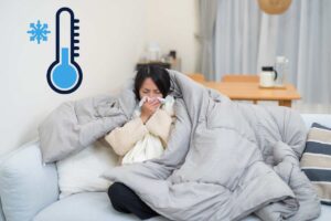 Una ragazza sul divano che sente freddo e si soffia il naso ed in altro a sinistra un termometro che segna una temperatura ghiacciata