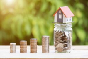 Casa su barattolo di vetro con monete, fila di monete impilate