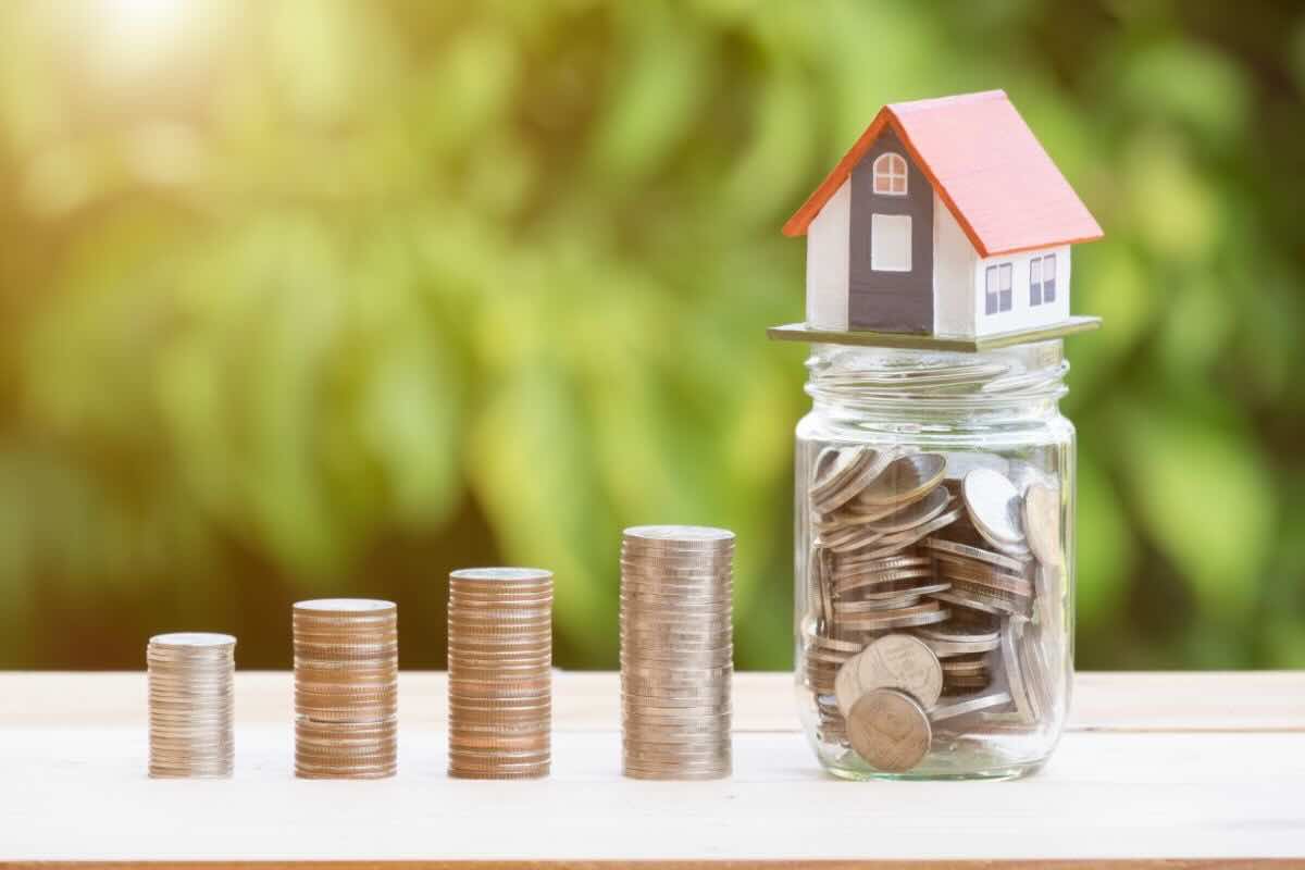 Casa su barattolo di vetro con monete, fila di monete impilate