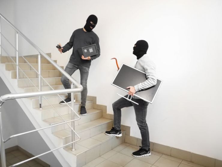ladri che salgono le scale con un televisore e una piccola cassaforte in mano