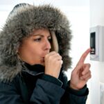 Una persona che imposta il termostato perché sente freddo e indossa il cappotto.